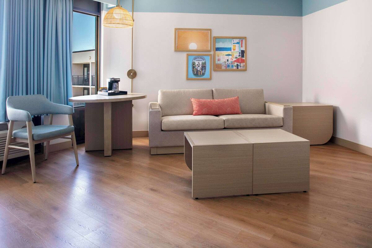 A modern living room with a sofa, a chair, a coffee table, and a dining area with a table and chairs.