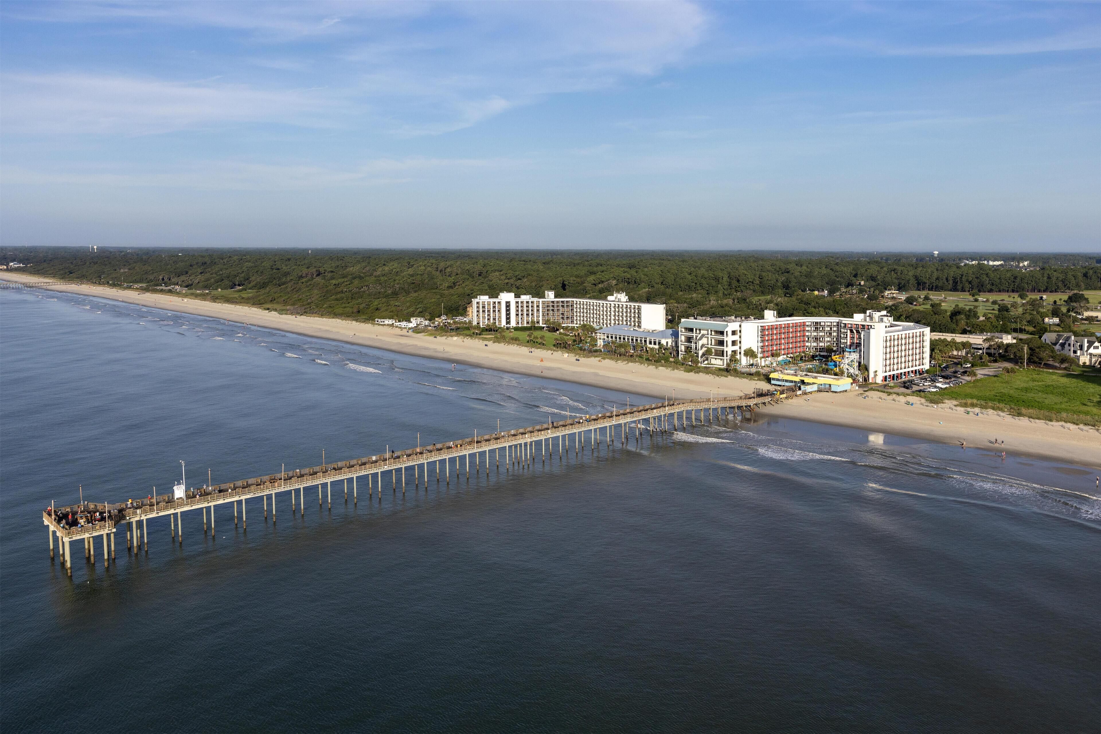 Un hotel frente al mar con un muelle que se adentra en el agua, habitaciones con vista a la playa y vistas al océano.