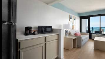 A modern kitchen with a microwave, coffee maker, and cabinets. There is a balcony with a view of the sea.