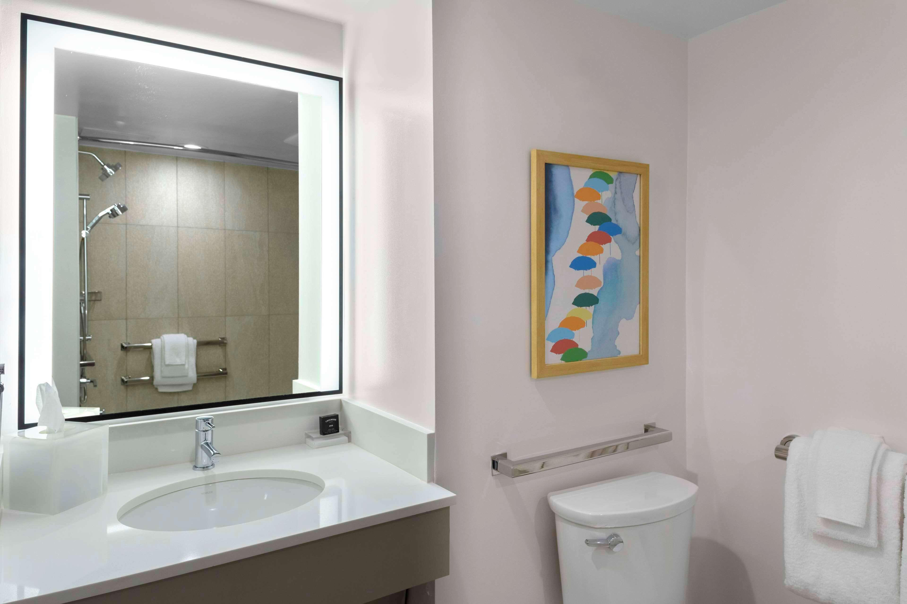 A modern bathroom with a large mirror, white sink, and toilet.