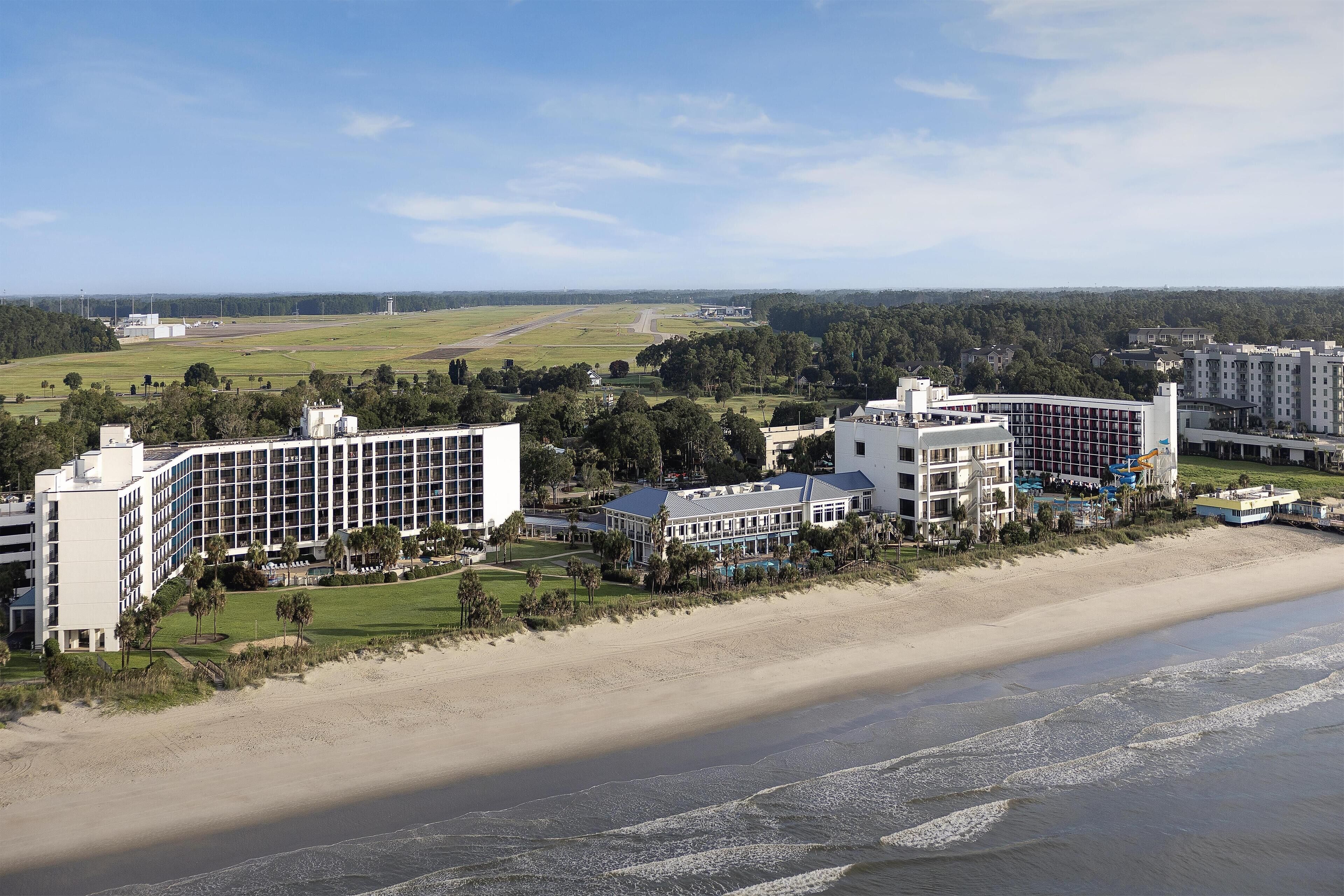 A coastal hotel with multiple buildings, a beach, and a golf course in the background.