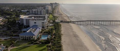 Un hotel frente al mar con vista a la playa, un muelle y una zona de piscina.