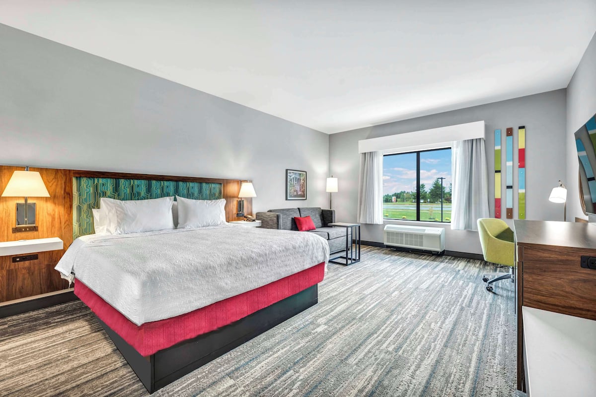 A hotel room with a large bed, a desk, a chair, and a window with a view of the outdoors.