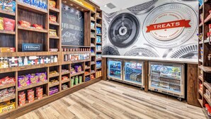 A hotel lobby with a 'Hilton Honors' sign, snack shelves, and a 'Welcome to Greensboro' banner.