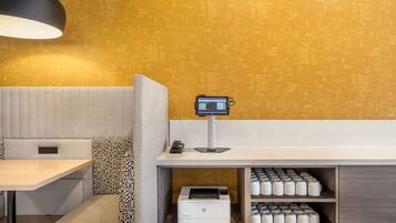 Habitación de hotel con sofá, una mesa, un escritorio con impresora y un monitor de computadora instalado en la pared.
