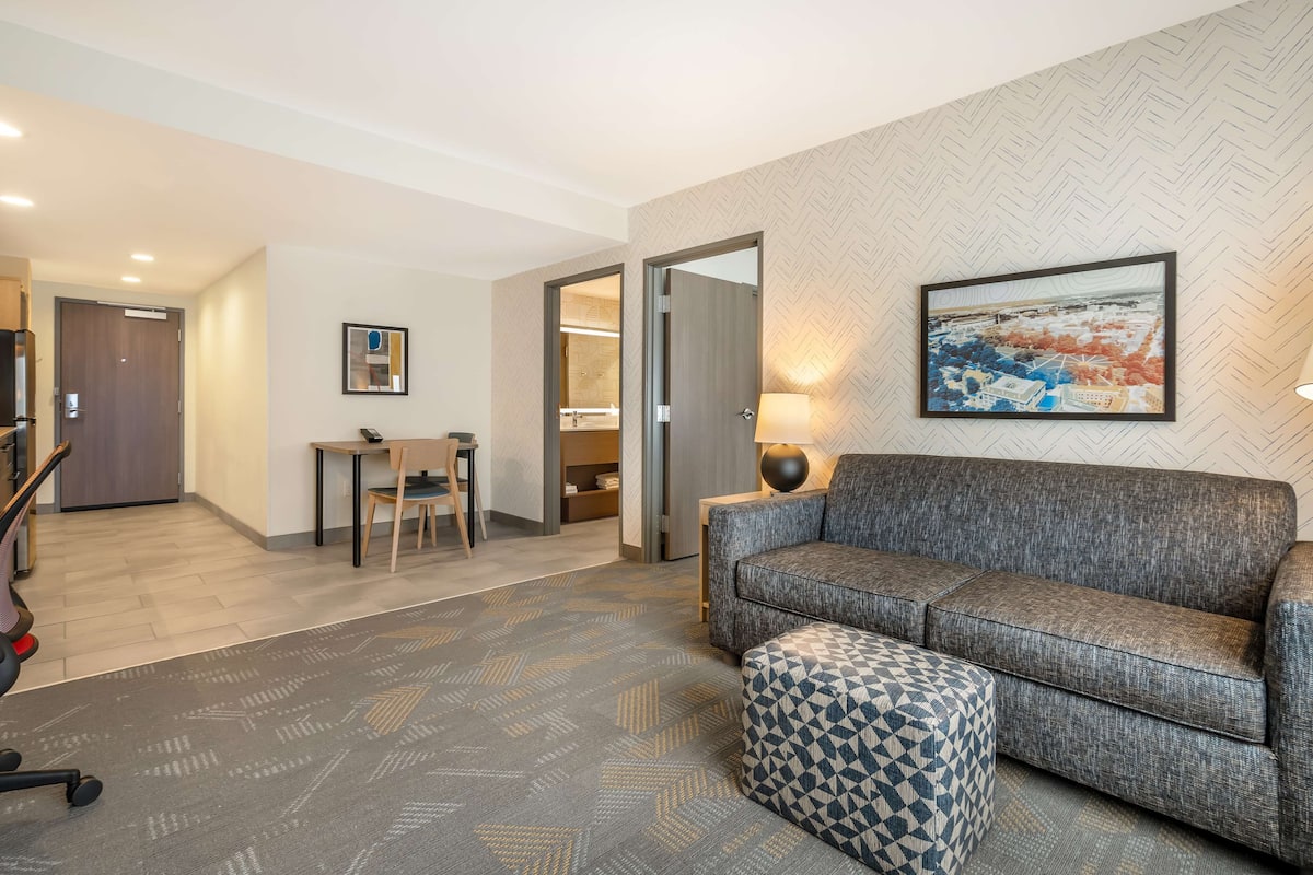 A modern living room with a grey sofa, ottoman, and a dining area with a table and chairs.