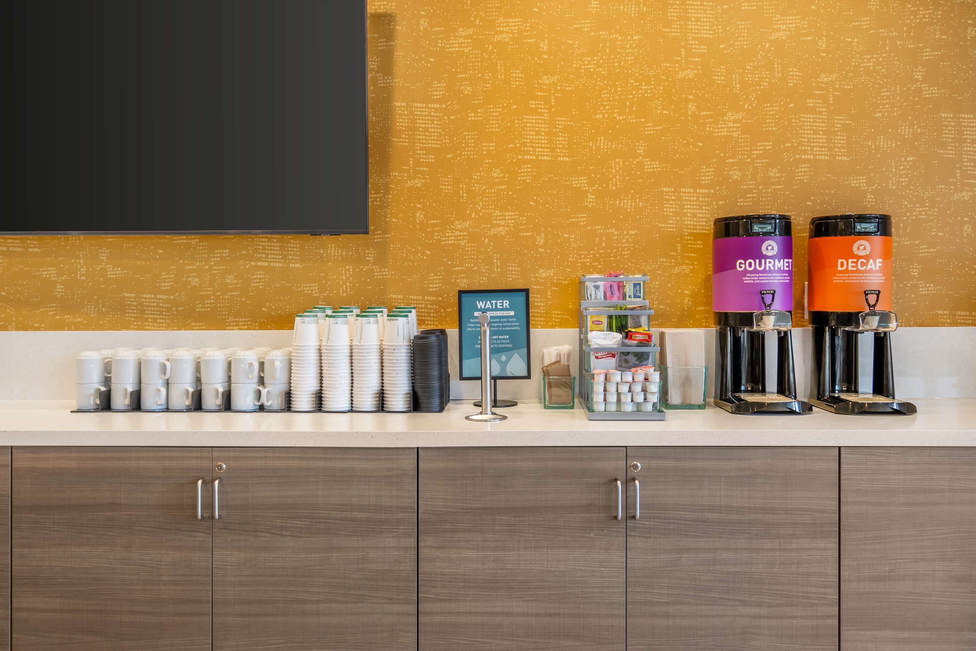 Zona de recepción de hotel con estación de café, dispensador de agua y un cartel que indica la disponibilidad de agua.
