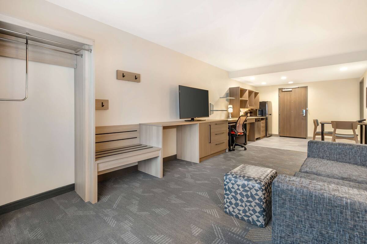A modern, compact living space with a kitchenette, a flat-screen TV, a sofa, and a bench.