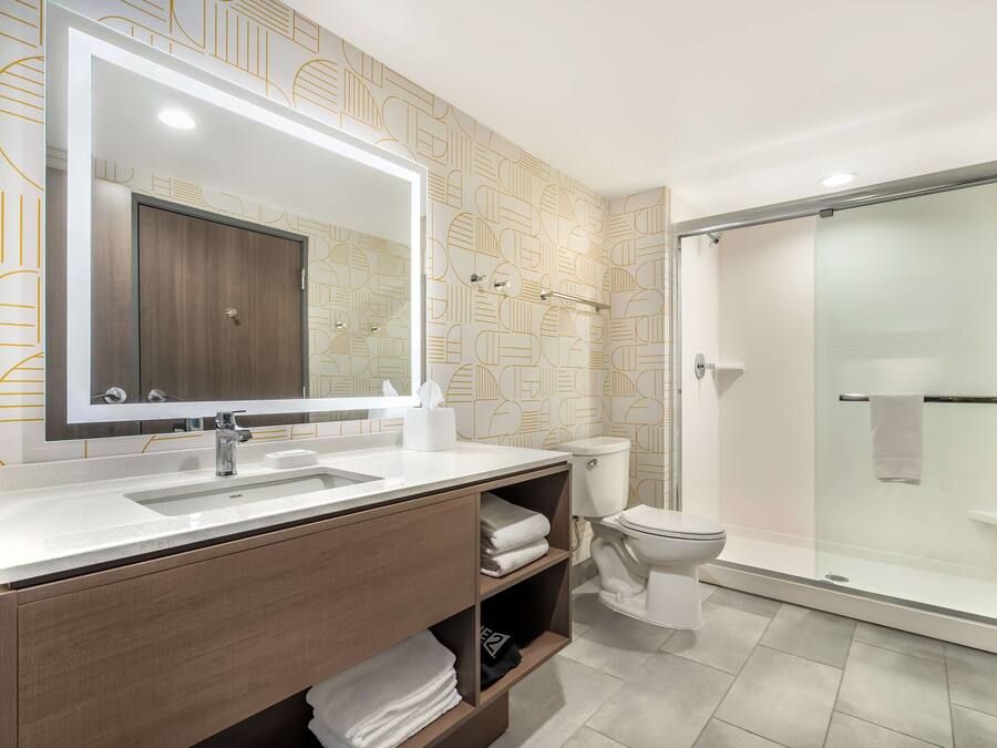 A modern bathroom with a large mirror, a shower, and a toilet.
