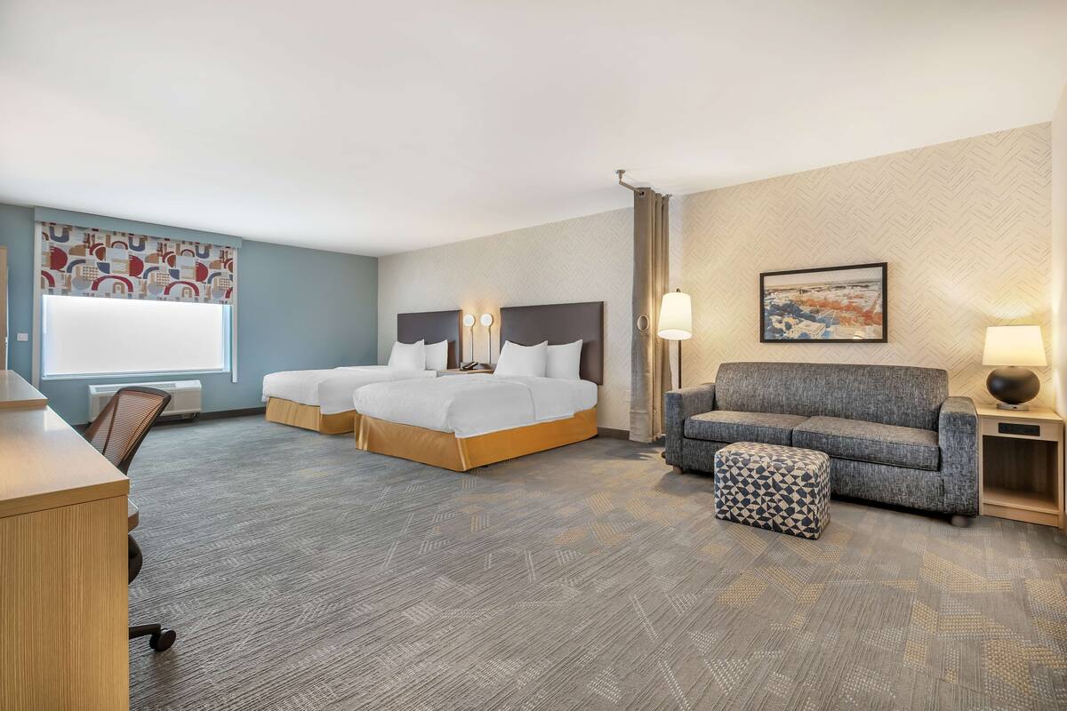 A hotel room with two beds, a sofa, an ottoman, a desk, and a chair.