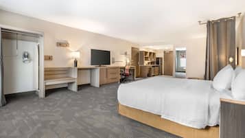A hotel room with a large bed, a desk with a chair, a TV, a wardrobe, and a bathroom with a shower and toilet.