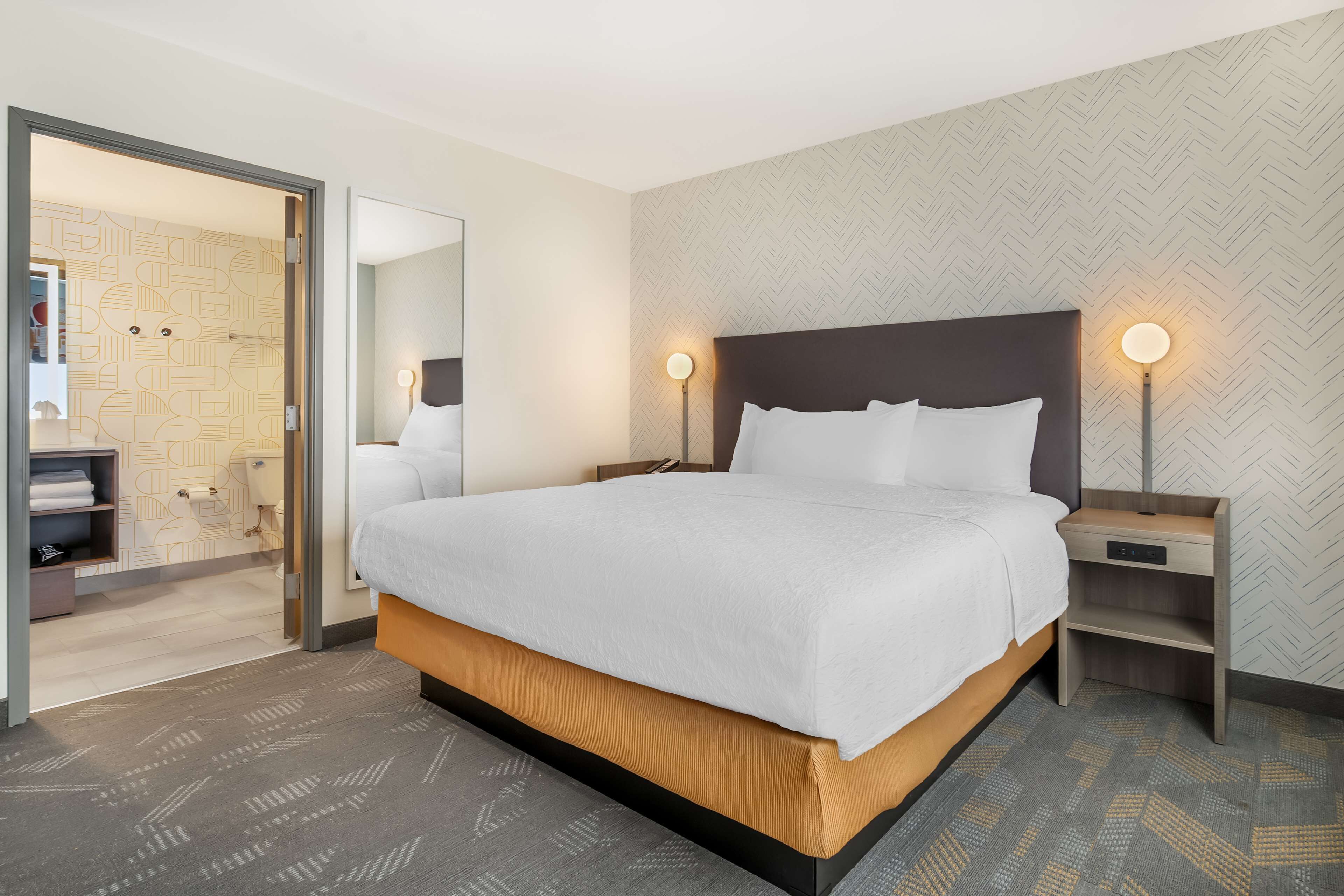 A modern hotel room with a large bed, bedside tables, and a mirror.