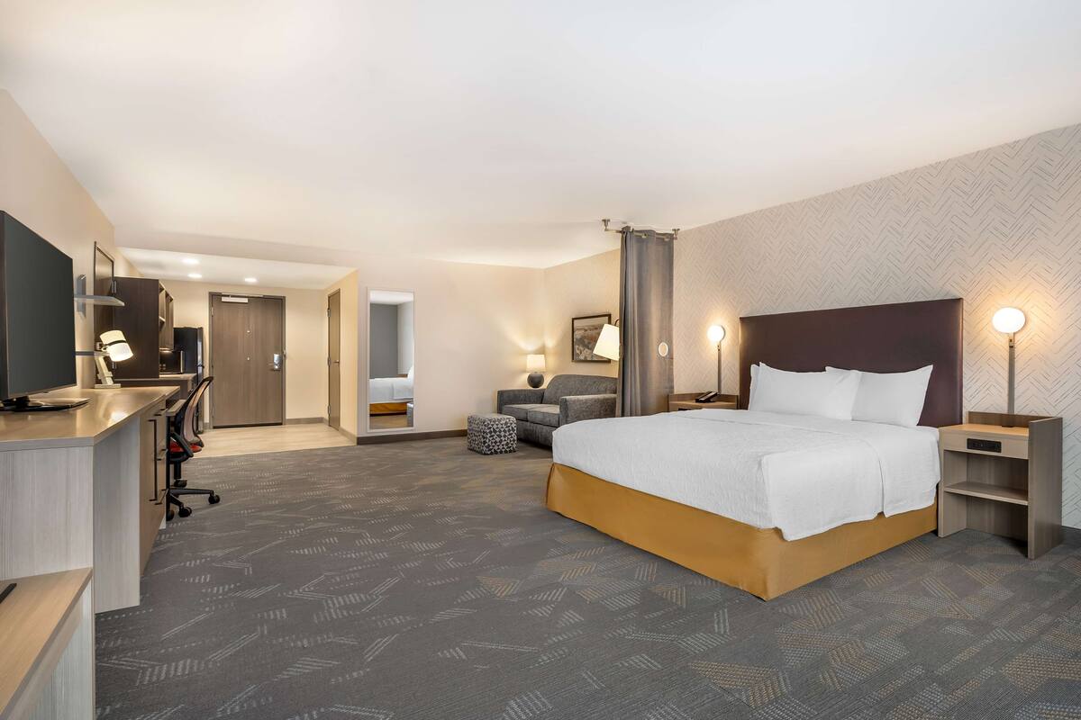 A hotel room with a large bed, a desk with a chair, a TV, and a bathroom visible through an open door.