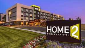 A modern hotel building with a sign reading "HOME 2 Suites by Hilton" and a well-maintained lawn with colorful flowers. - Home2 Suites By Hilton Reynoldsburg Columbus East (Reynoldsburg)