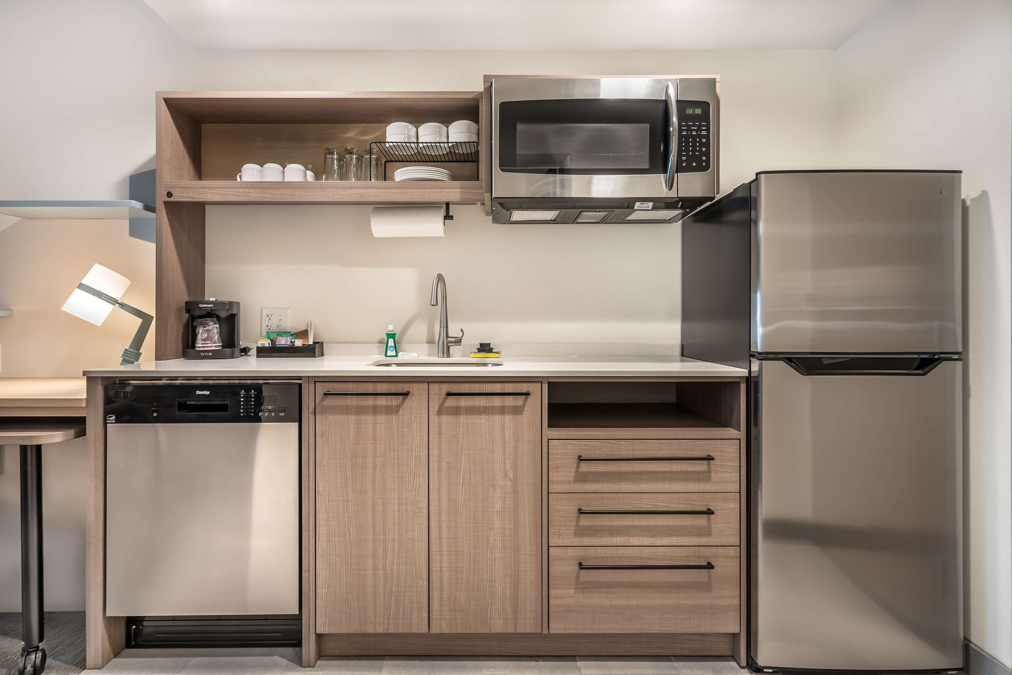 A modern kitchen with a dishwasher, microwave, refrigerator, and wooden cabinets.