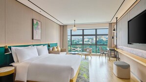 Ein modernes Hotelzimmer mit einem großen Bett, einem Fernseher, einem Schreibtisch und Blick auf die Stadt.