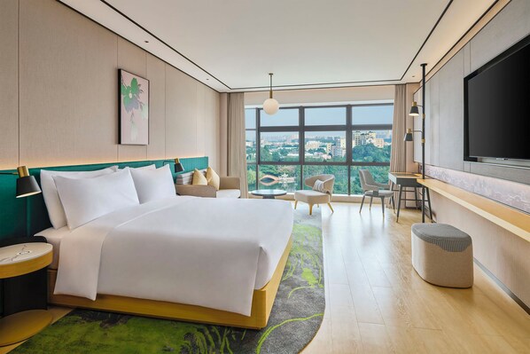 Habitación de hotel moderna con una cama grande, televisión, escritorio y vistas a la ciudad.