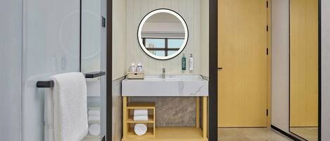 A modern bathroom with a glass shower enclosure, a wooden vanity with a marble countertop, and a round mirror.