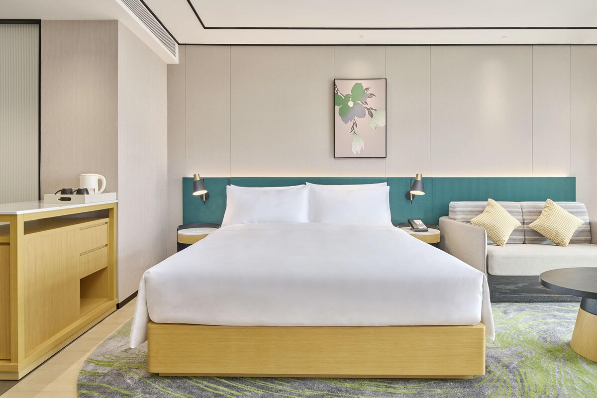 A hotel room with a bed, a desk, a chair, a sofa, and a small table.