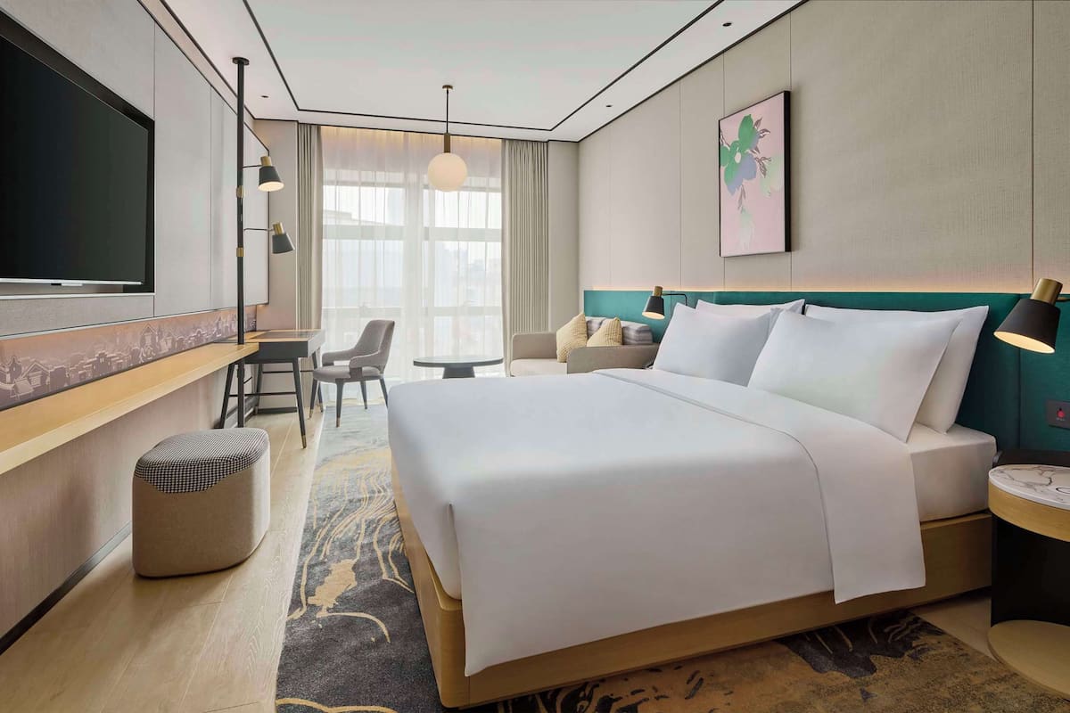 A hotel room with a large bed, a desk, a chair, a TV, and a window with curtains.