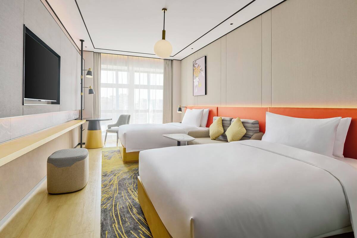 A hotel room with a large bed, a smaller bed, a desk, a chair, and a TV mounted on the wall.