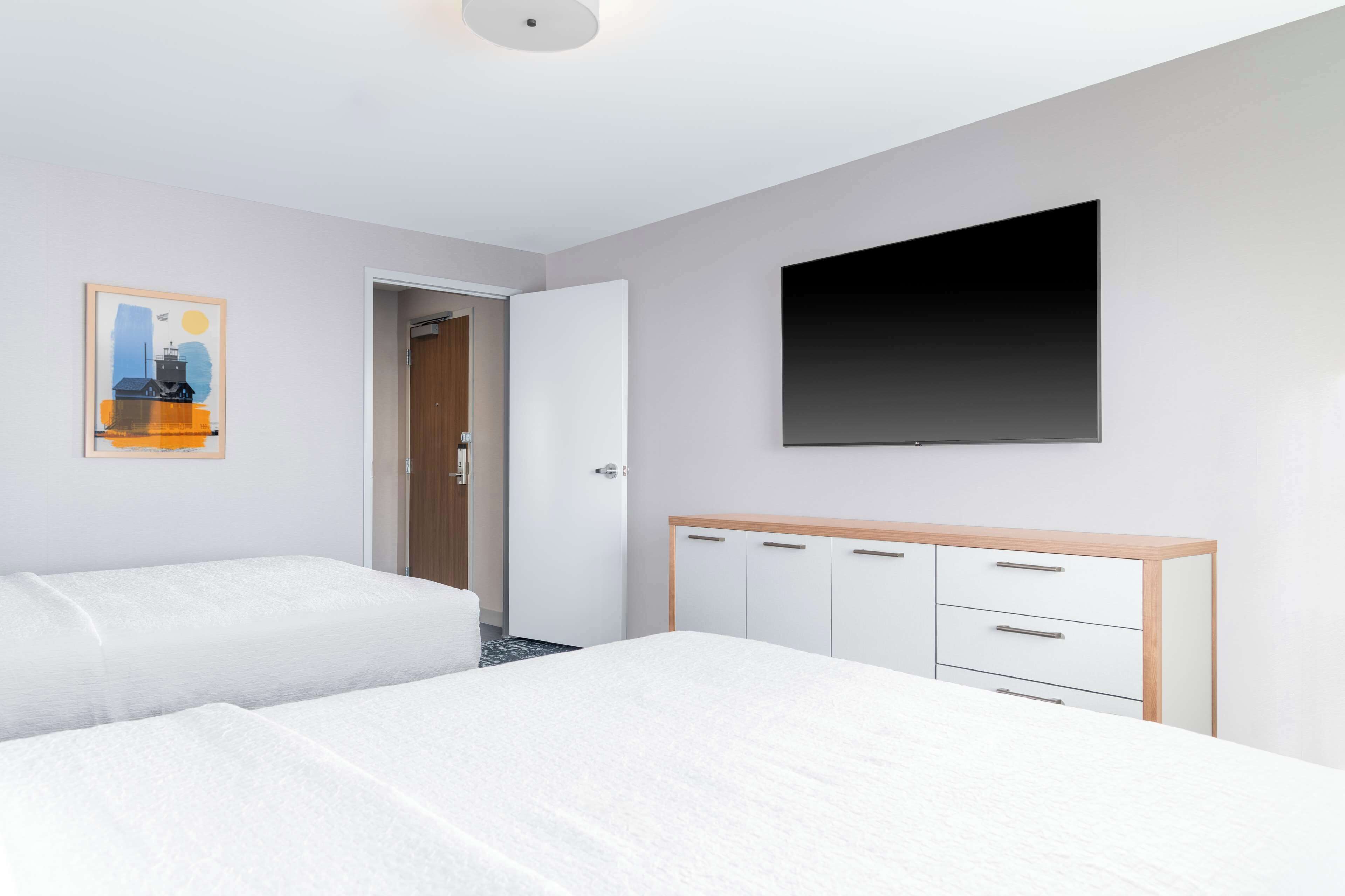 Una habitación de hotel con dos camas, un armario, un cuadro y un televisor.