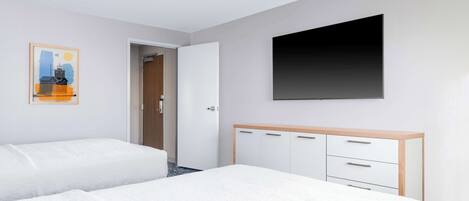 Una habitación de hotel con dos camas, un armario, un cuadro y un televisor.