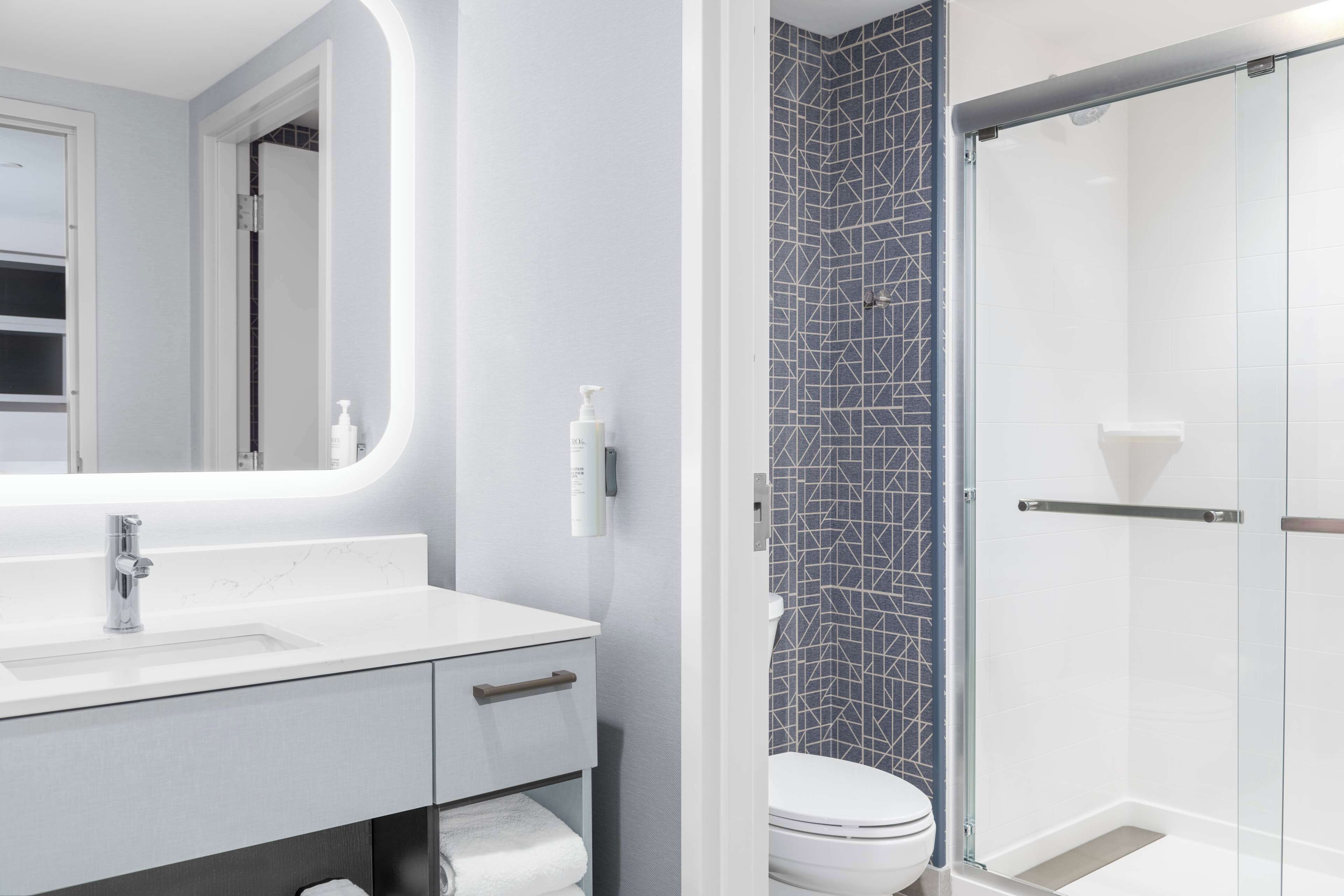 A modern bathroom with a white vanity, a large mirror, a glass shower enclosure, and a toilet.