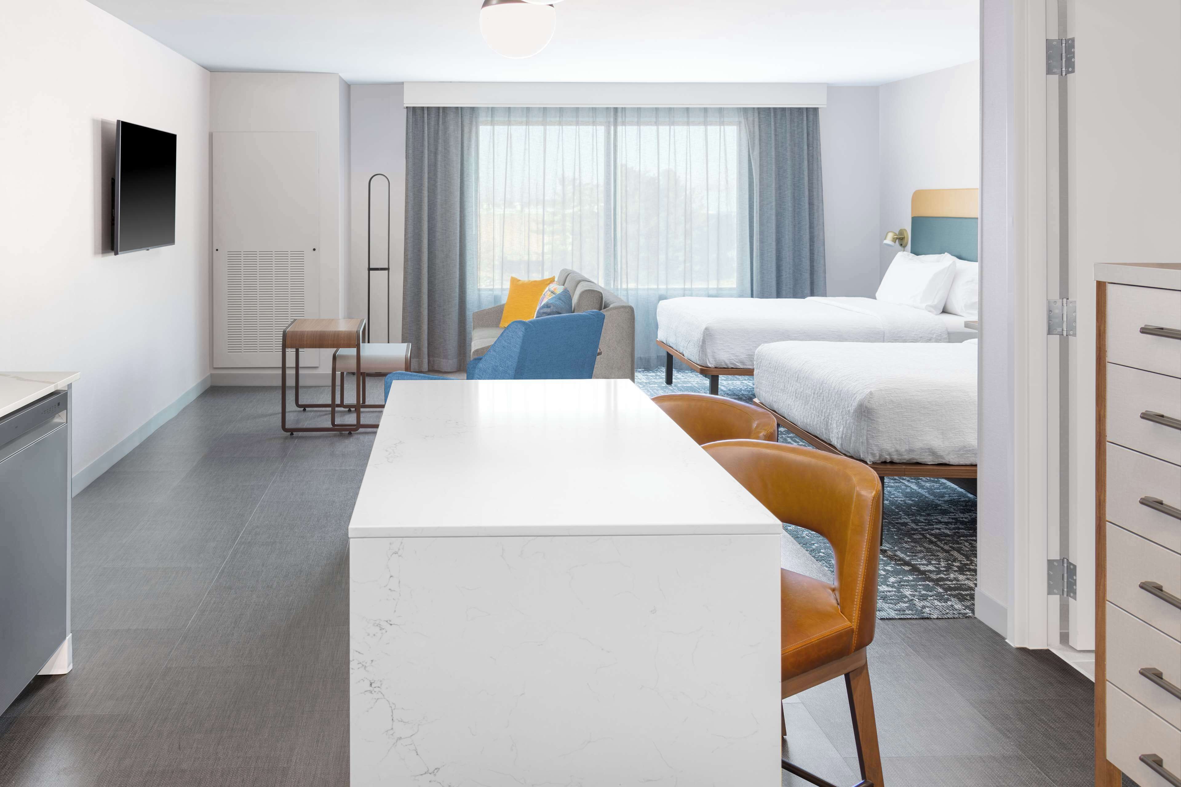 A hotel room with a white marble desk, two beds, a TV, and a window with curtains.
