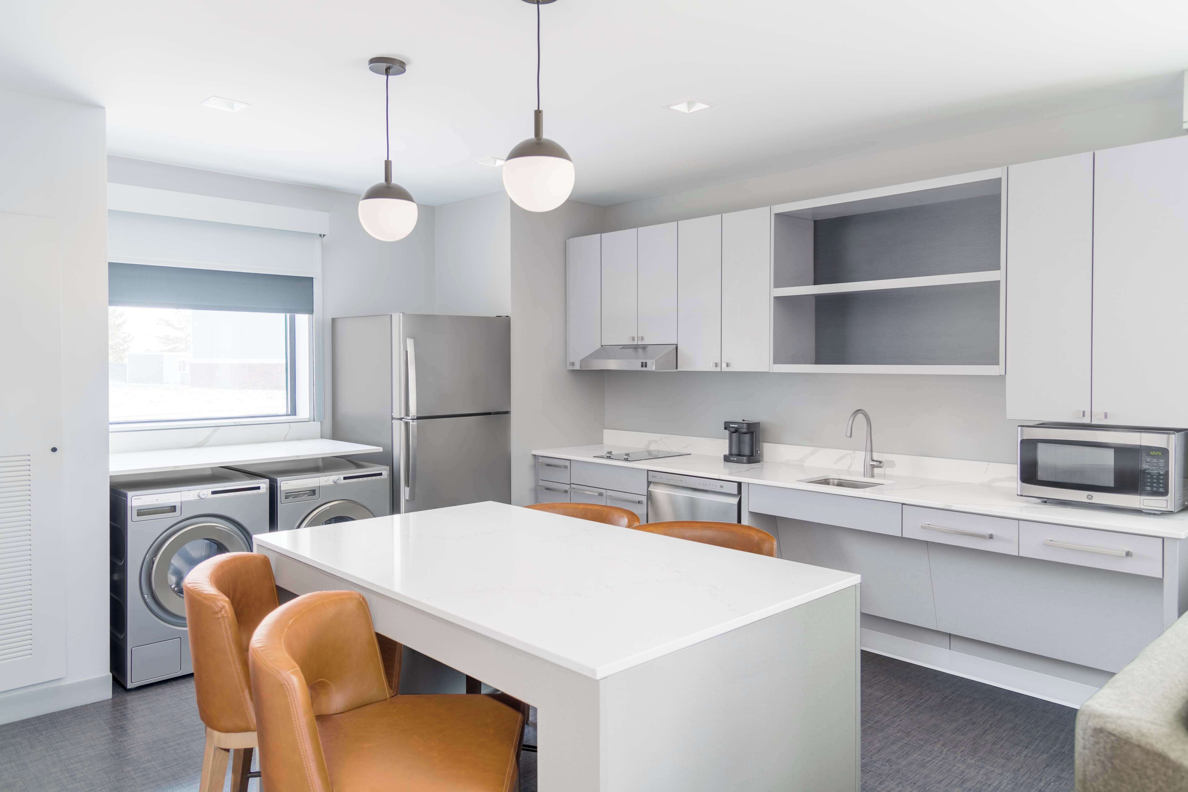 Une cuisine moderne dotée d’un îlot central, d’appareils électroménagers intégrés et de luminaires suspendus.