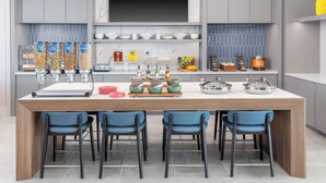 A modern kitchen with a central island, four blue chairs, and various kitchen items. - Homewood Suites Holland (Holland)