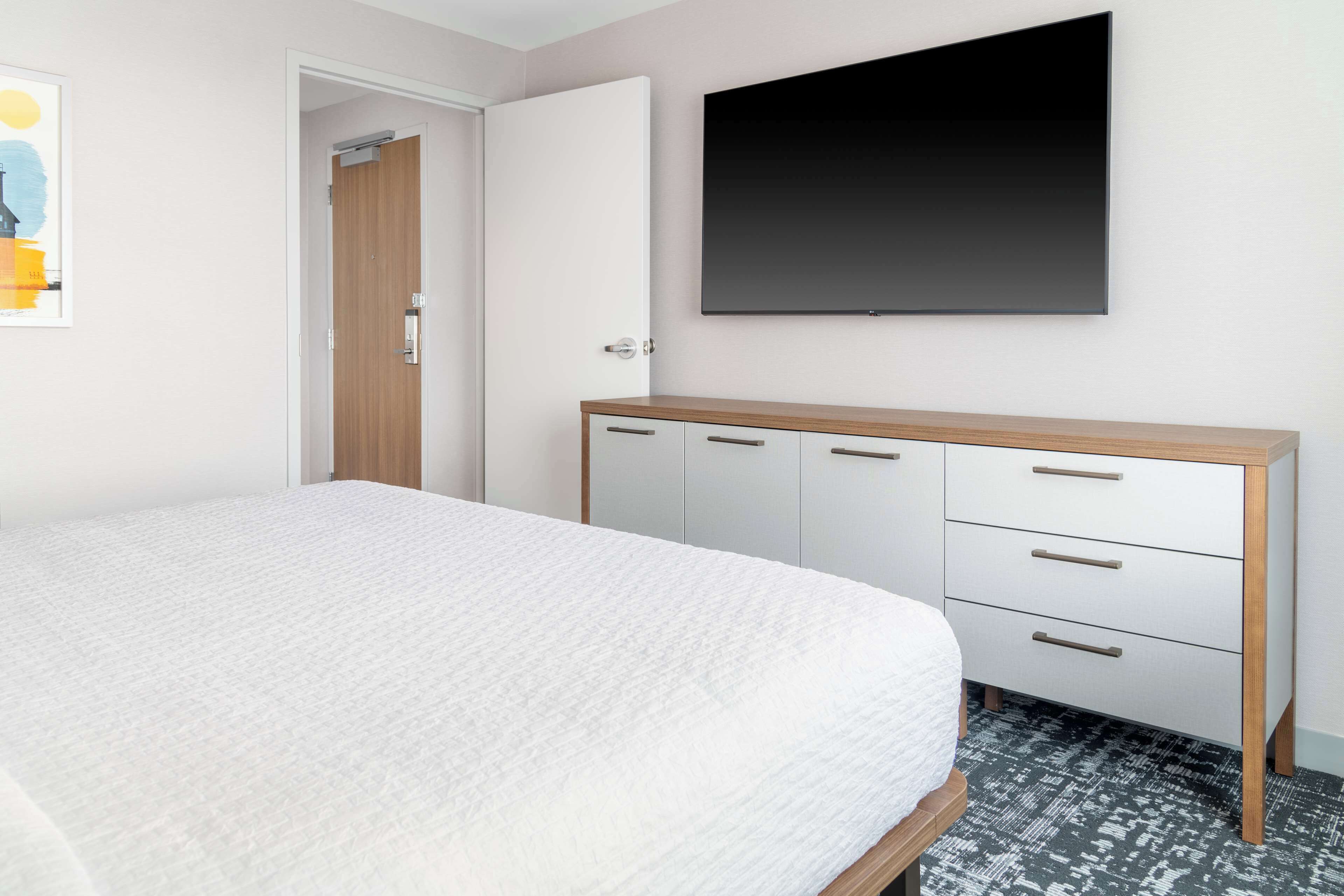 Ein Schlafzimmer mit einem Bett, einem Kleiderschrank, einem flachbildfernseher an der Wand und einer Tür zu einem anderen Raum.