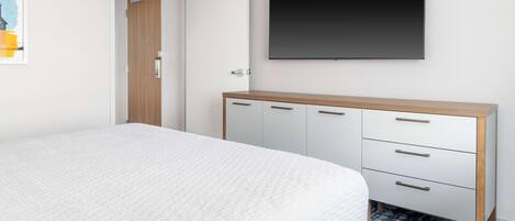 Ein Schlafzimmer mit einem Bett, einem Kleiderschrank, einem flachbildfernseher an der Wand und einer Tür zu einem anderen Raum.