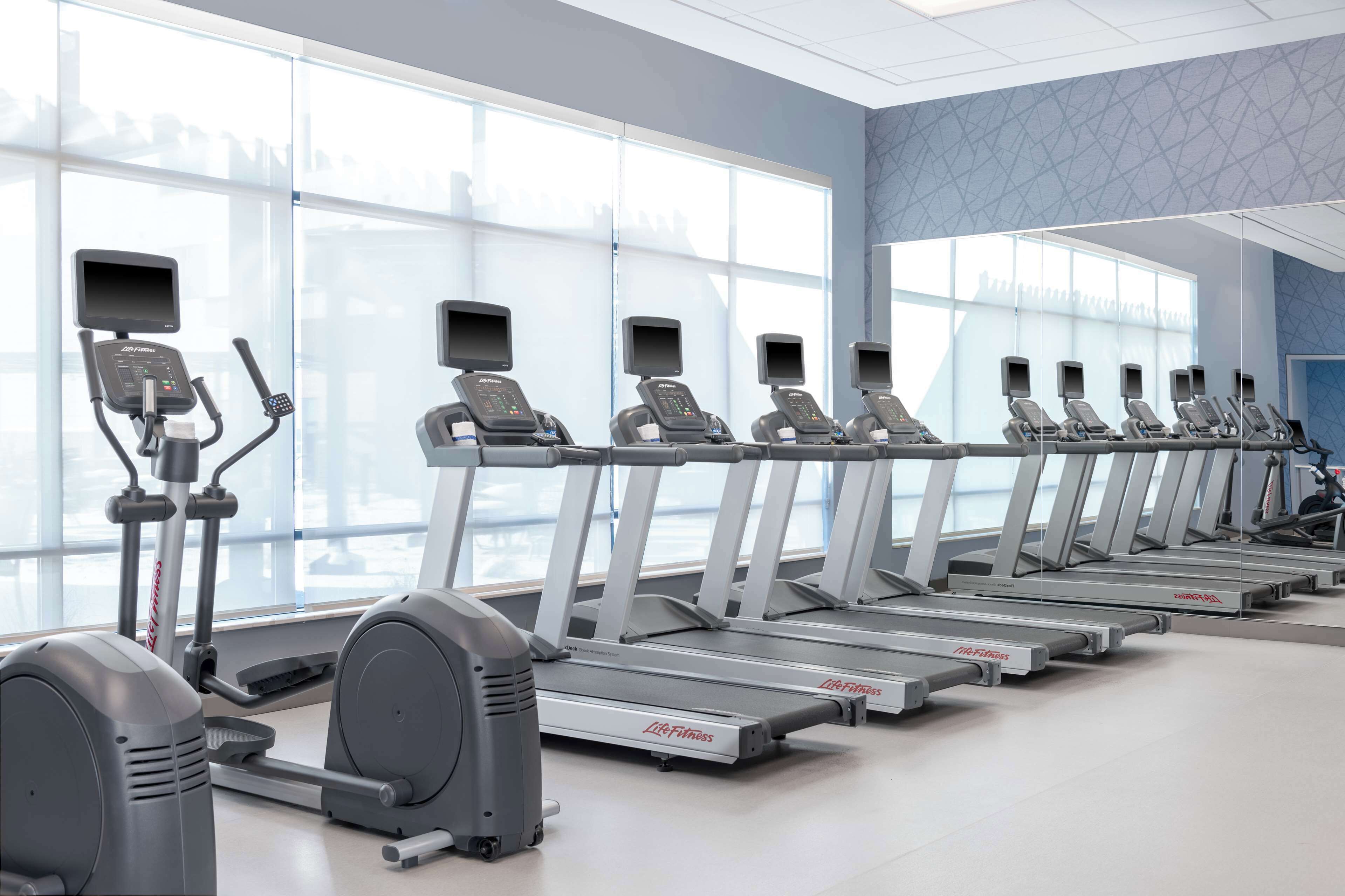 A fitness center with multiple treadmills and elliptical machines arranged in a row.