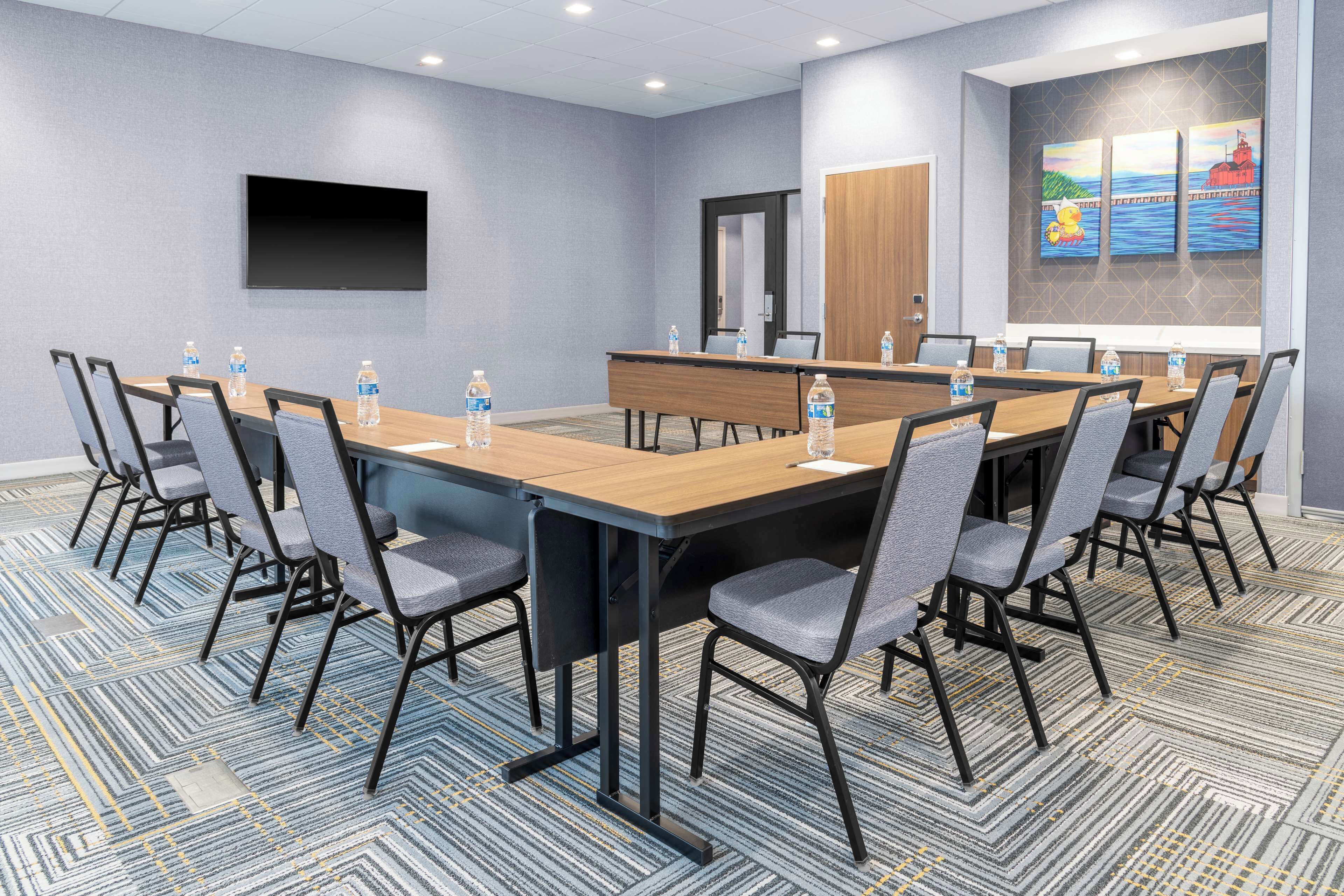 A conference room with a long table, chairs, water bottles, a flat-screen TV, and artwork on the wall.