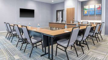 A conference room with a long table, chairs, water bottles, a flat-screen TV, and artwork on the wall.