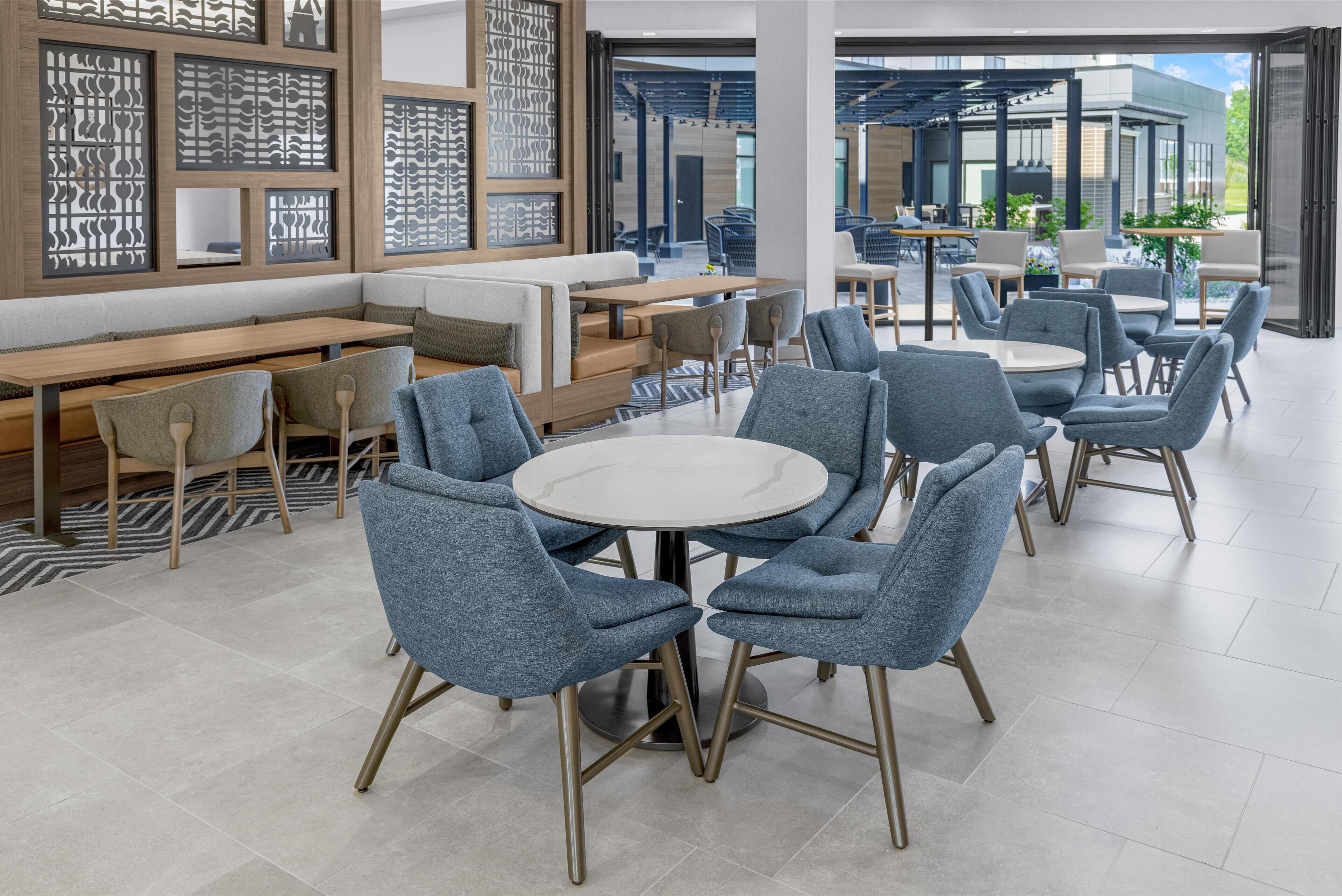 Ein modernes Restaurant mit runden Tischen, blauen Stühlen und Holzbänken, sowie dekorativen Trennwänden.