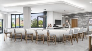 A modern bar area with a long counter, multiple bar stools, and a large window offering a view of the outside. - Homewood Suites Holland (Holland)