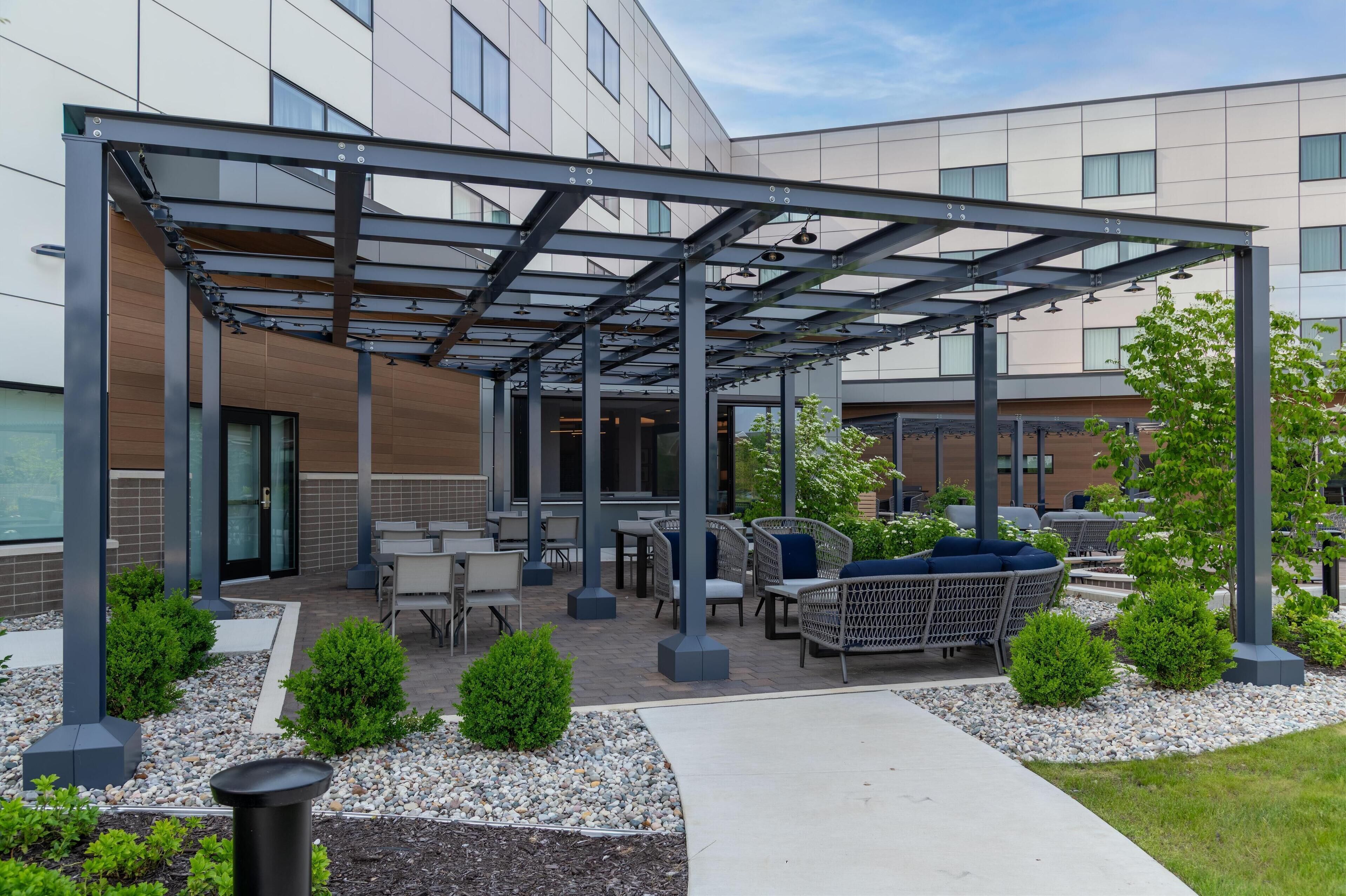 An outdoor patio area with seating, a pergola structure, and a building in the background.