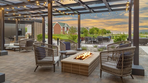 An outdoor patio with wicker furniture, a built-in fire feature, and string lights. - Homewood Suites Holland (Holland)
