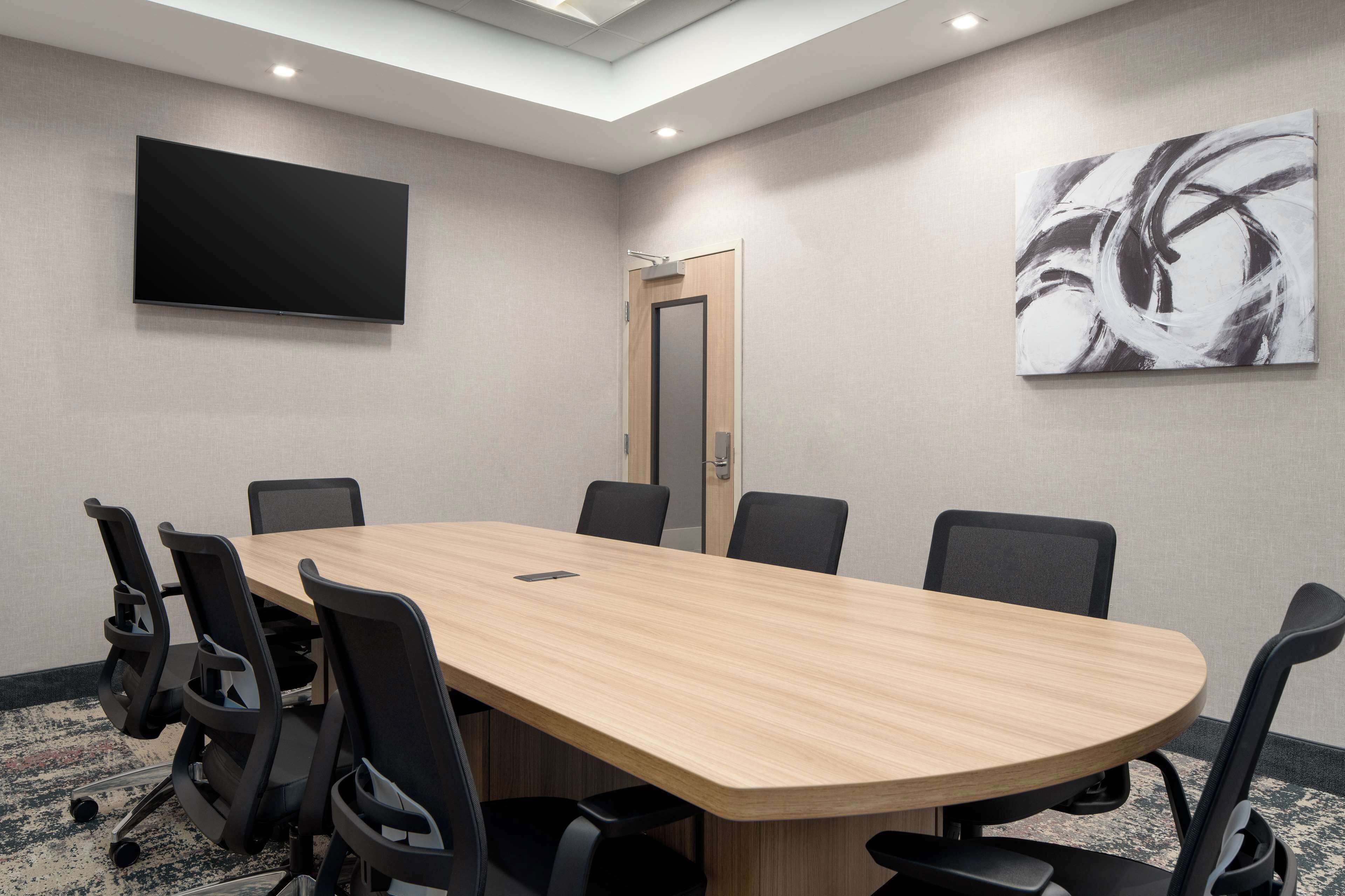 A conference room with a long table, six chairs, a flat-screen TV, and a large abstract painting on the wall.