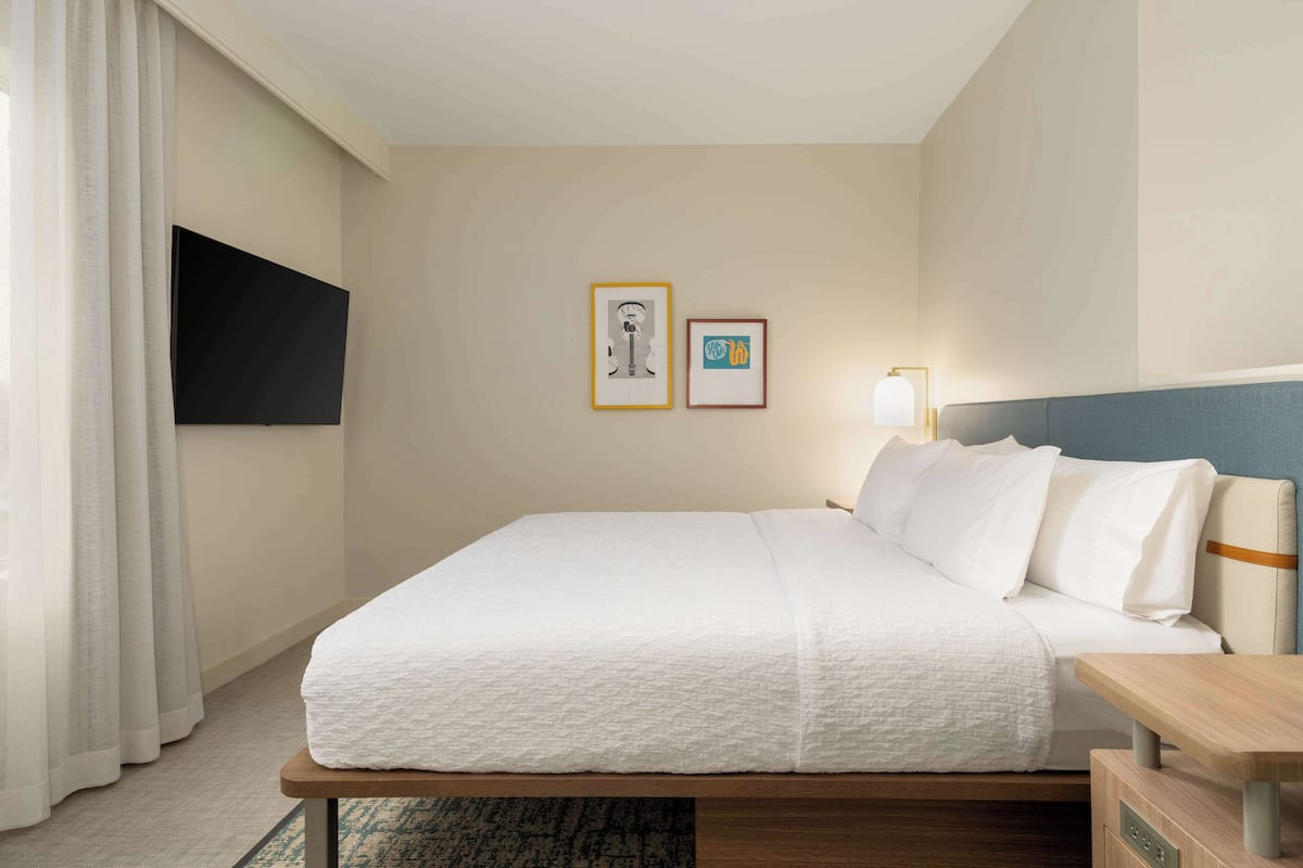 A hotel room with a bed, a bedside table, a lamp, and two framed pictures on the wall.