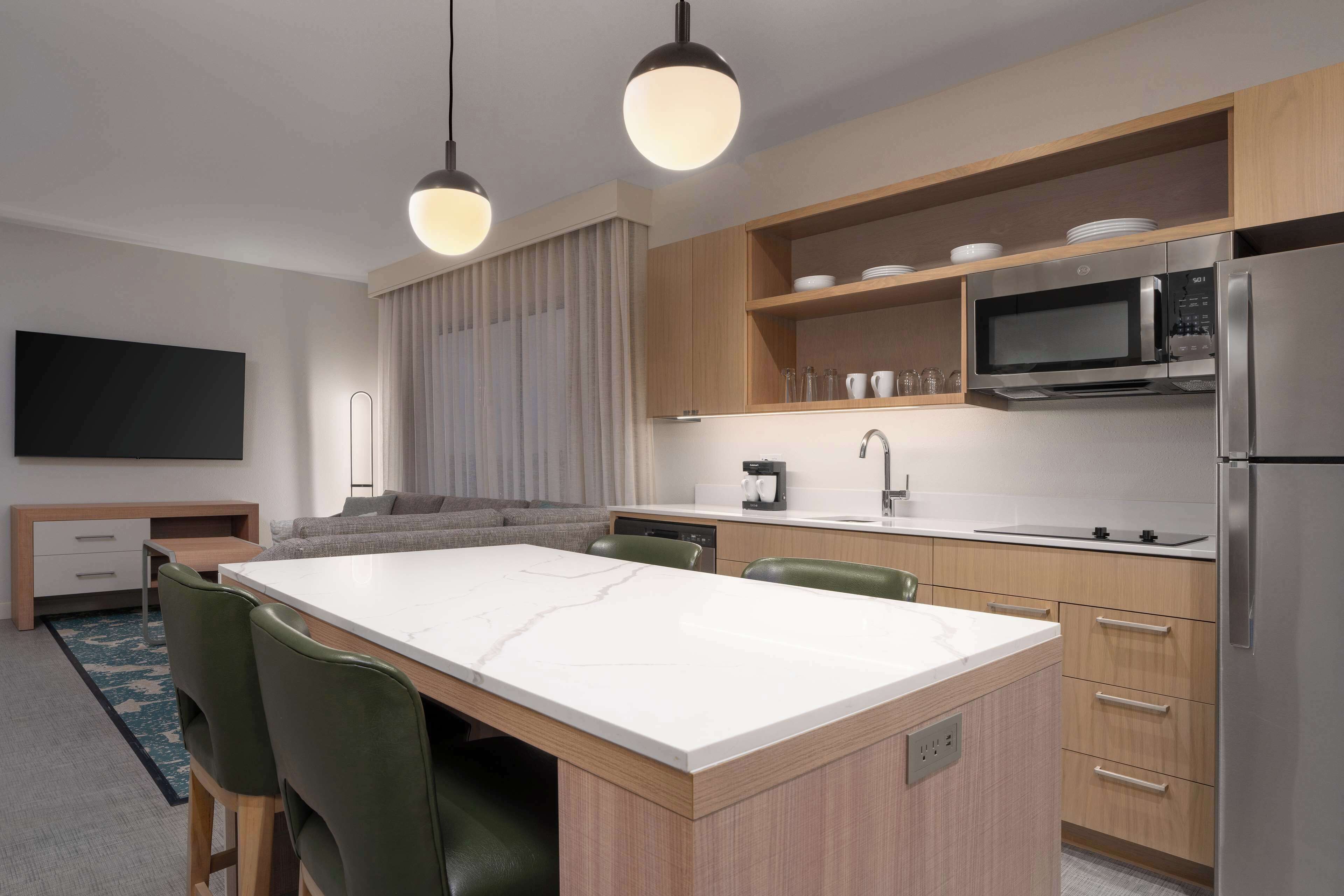 Una cucina moderna con isola centrale, mobili in legno, forno a microonde integrato e frigorifero in acciaio inox.