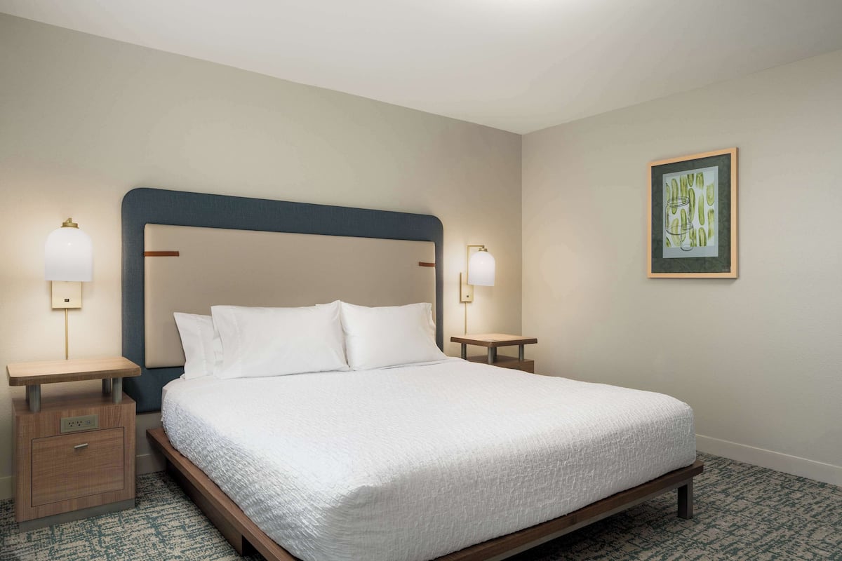 A neatly made bed with white linens, two bedside tables with lamps, and a framed artwork on the wall.