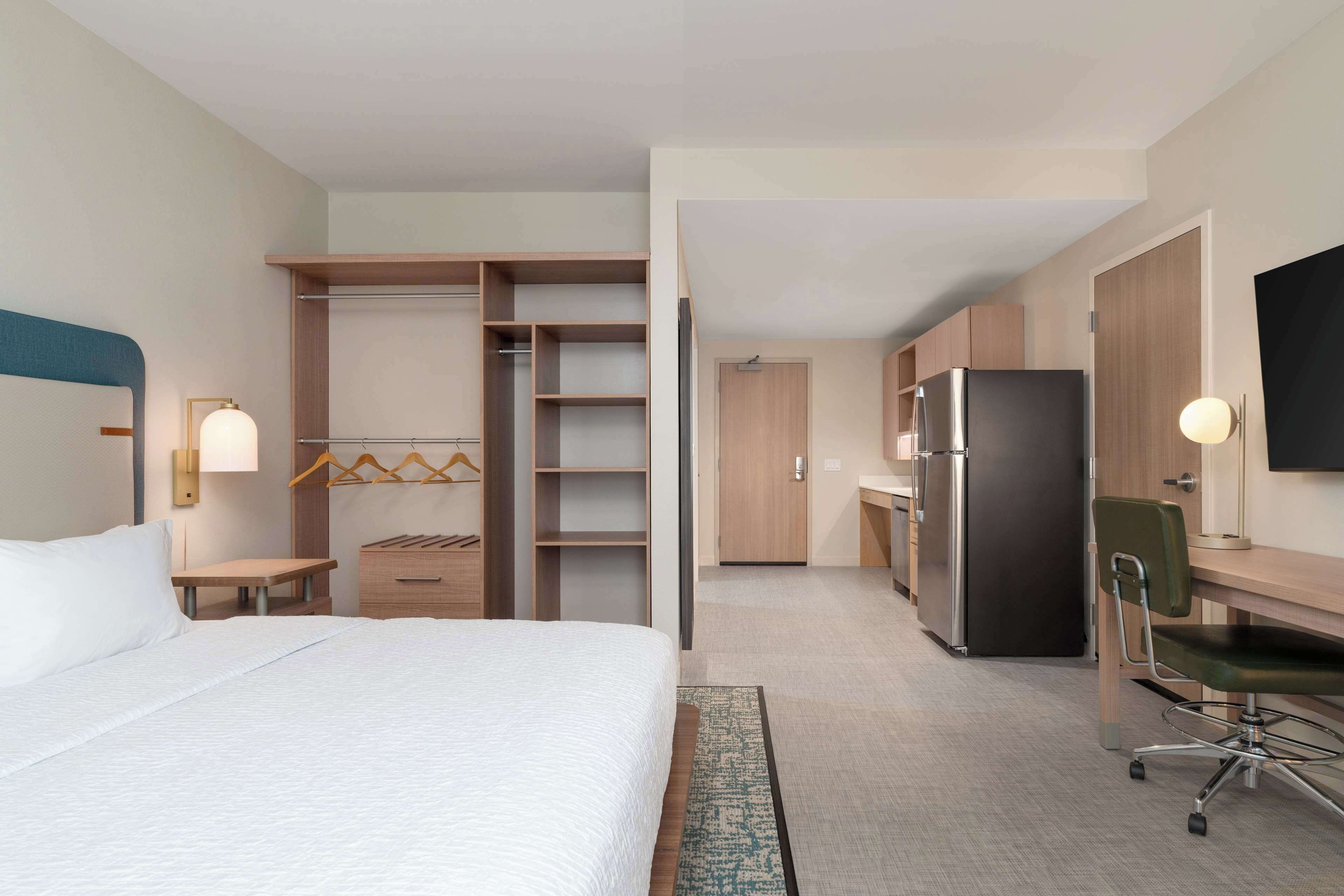 A hotel room with a bed, a desk, a refrigerator, a TV, and a walk-in closet.