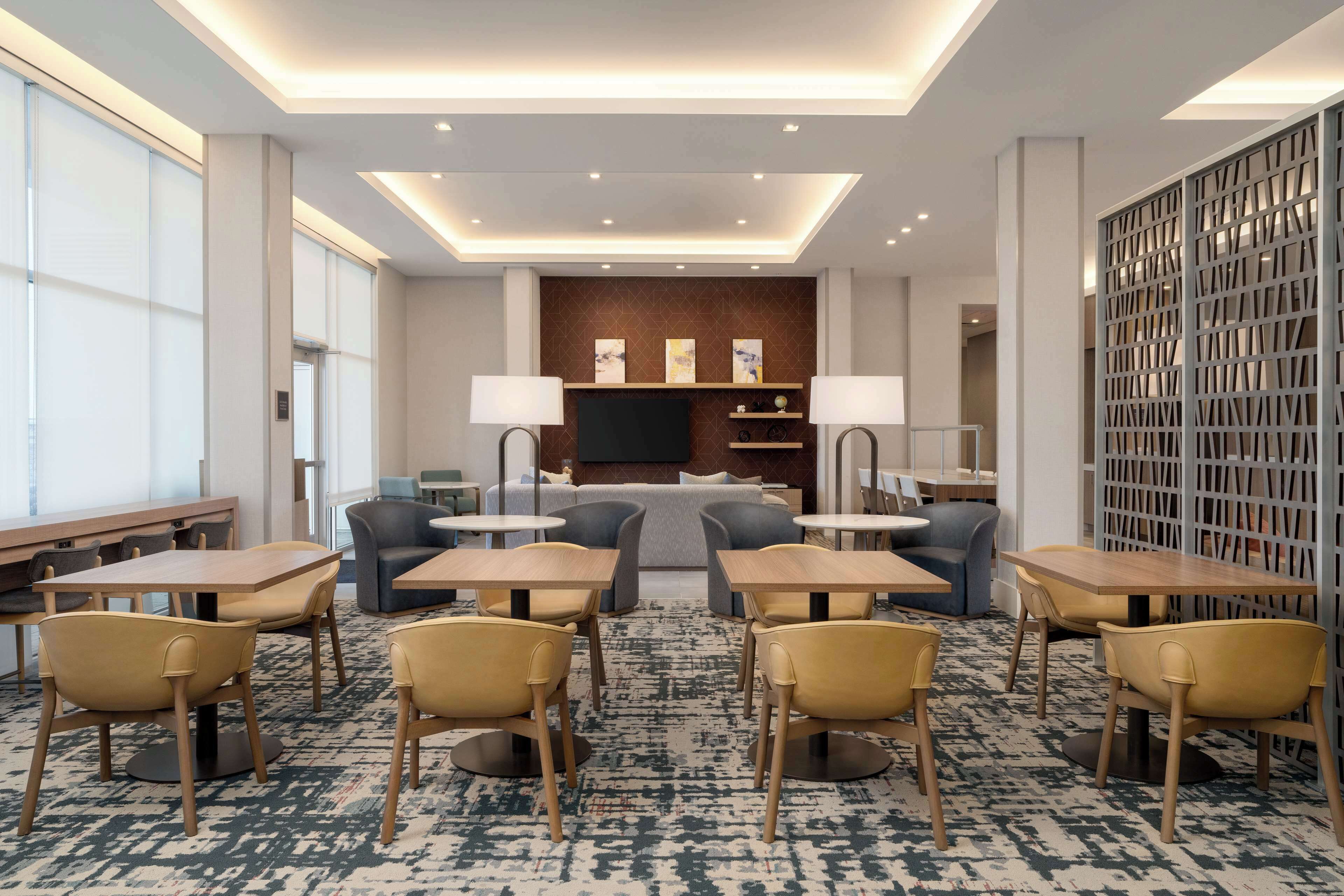 A modern hotel lobby with a seating area, tables, and a television screen.