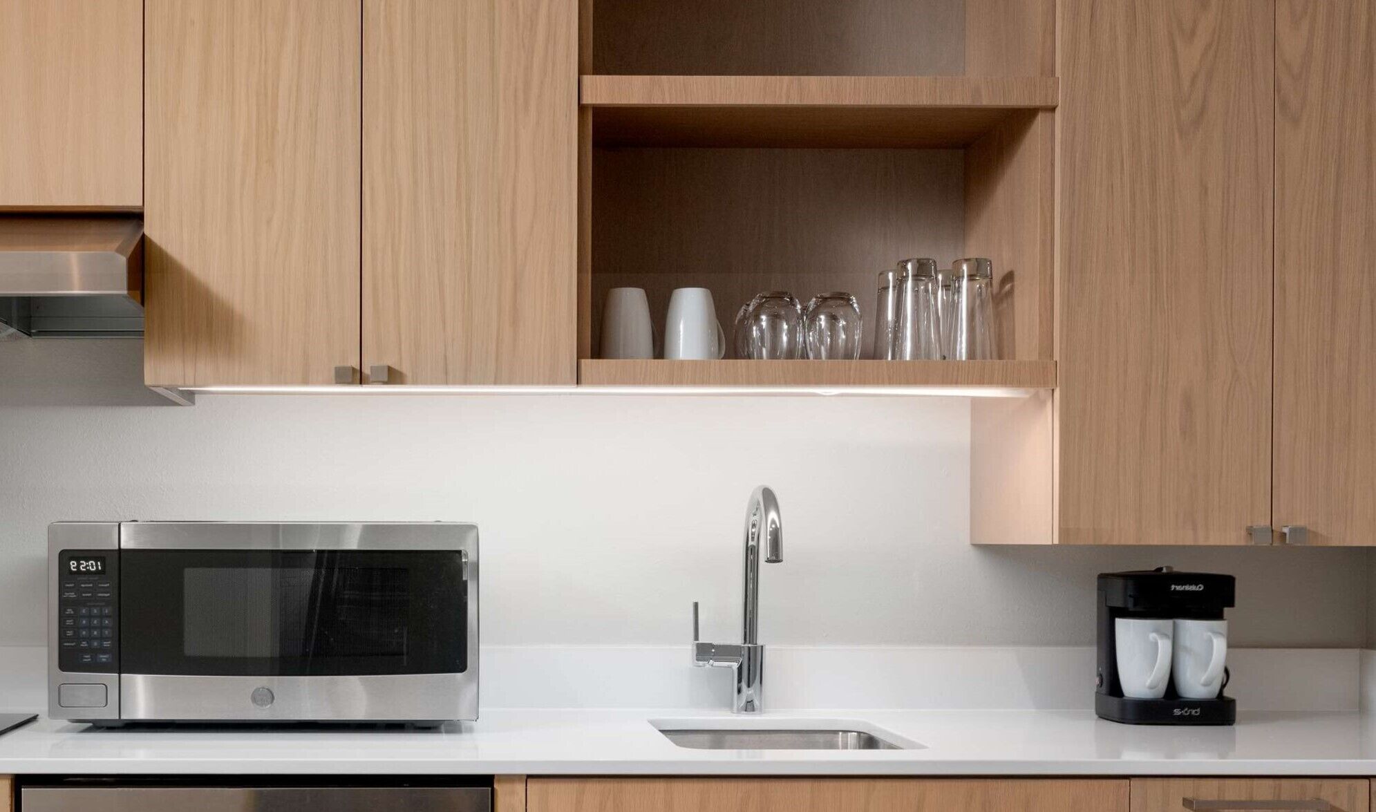 Una cocina moderna con un microondas de acero inoxidable, un lavamanos y una cafetera.