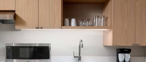 Una cocina moderna con un microondas de acero inoxidable, un lavamanos y una cafetera.