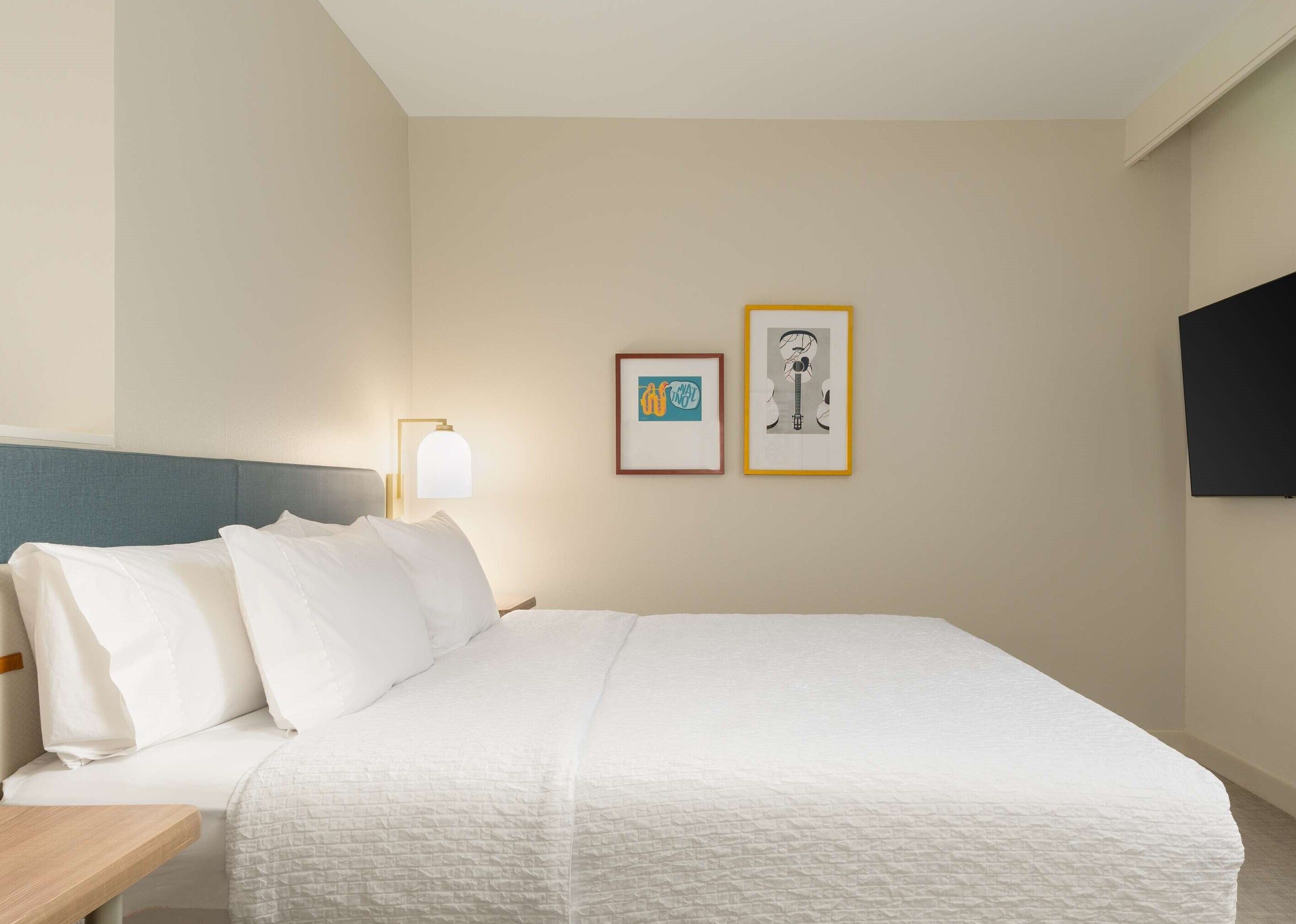 A hotel room with a bed, a bedside table, a lamp, and two framed pictures on the wall.
