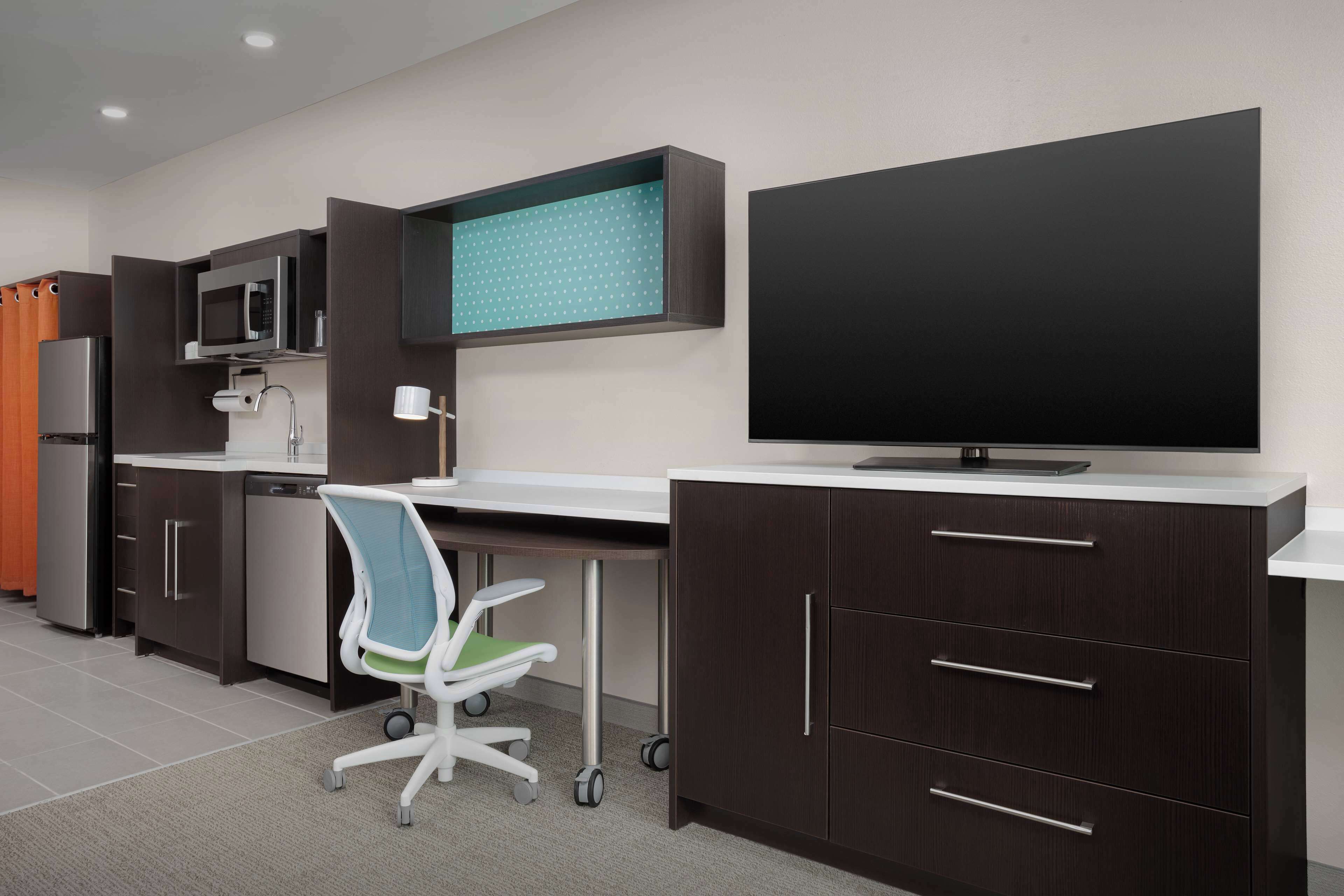 A modern kitchen with dark cabinetry, a microwave, a sink, and a large flat-screen TV mounted on the wall.